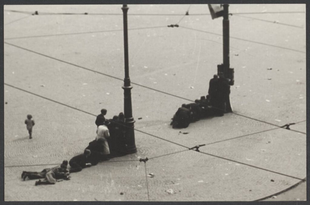 Mensen zoeken dekking op de Dam. Links loopt een een klein meisje over het plein.